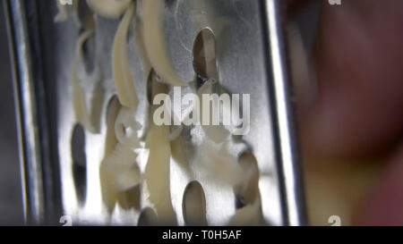 Macro colpo di mano gialla a reticolo di formaggio con una grattugia di metallo. Primo piano Foto Stock