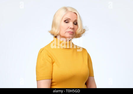 Triste senior donna bionda in abiti di colore giallo Foto Stock