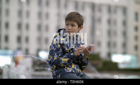 Spaventato ragazzo utilizza il telefono guardando attentamente Foto Stock