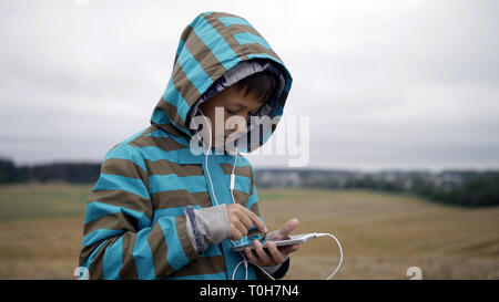 Ragazzo ascoltare musica dal tuo telefono, ragazzo in un campo sulla montagna di sera Foto Stock