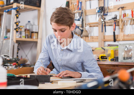 Bello adolescente britannico sorridente e la lavorazione del legno in officina Foto Stock