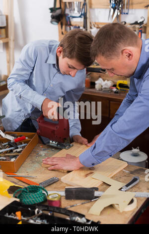 Ritratto di padre e figlio il taglio di tavolato in legno con Seghetto da traforo nel luogo di lavoro Foto Stock