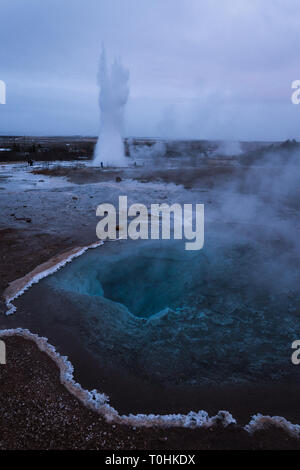 Strokkur geyser sta scoppiando per la distanza con la limpida acqua di Blesi geyser in primo piano, disegno il tuo occhio nella sua crystal clear profondità! Foto Stock