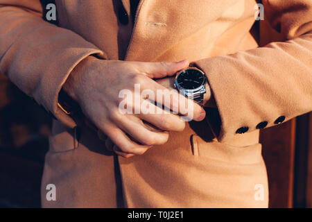 Giovane uomo tempo di controllo sul metallo elegante mano meccanica guarda in attesa di una riunione all'esterno. Accessori maschio Foto Stock