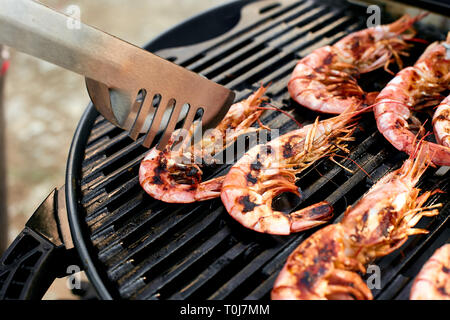 L'uomo la cottura la grigliatura grande tiger gamberi in padella per grigliare, vista dall'alto. Pesce alla griglia. Barbecue gamberetti. Foto Stock