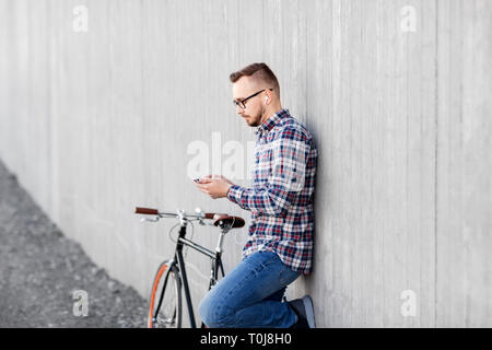 Hipster uomo in auricolari con smartphone e bici Foto Stock