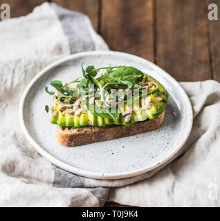 Verde sandwich sano realizzato da spinaci, germogli, avocado e diversi semi su una piastra bianca Foto Stock