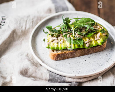 Verde sandwich sano realizzato da spinaci, germogli, avocado e diversi semi su una piastra bianca Foto Stock