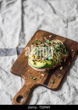 Verde sandwich sano realizzato da spinaci, germogli, avocadi e diversi semi su un pannello di legno Foto Stock