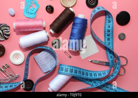 Un set di strumenti per il sarto - filettatura, forbici, perni, bobine, aghi, metro di misura. Su uno sfondo di colore rosa. Flatlay. Foto Stock