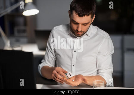 Imprenditore prendere pillole medicinali di notte office Foto Stock