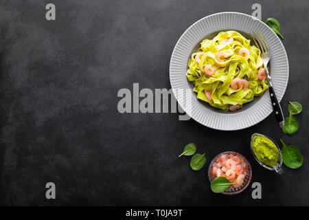 Bollito di fettuccine con spinaci freschi pesto e gamberetti su sfondo nero. Cucina Italiana. Piatto sano per il pranzo. Vista superiore Foto Stock