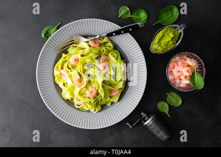 Bollito di fettuccine con spinaci freschi pesto e gamberetti su sfondo nero. Cucina Italiana. Piatto sano per il pranzo. Vista superiore Foto Stock