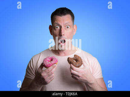 Uomo caucasico con marrone e ciambelle rosa su sfondo blu Foto Stock