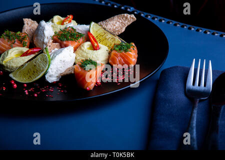 Deliziosi salmone con patè e hummus nel ristorante dello sfondo. Sano cibo esclusivo sul grande piatto nero closeup Foto Stock