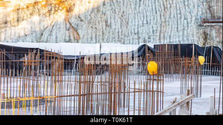 In cemento armato, in costruzione. Colonne di barre di acciaio di rinforzo e hardhats giallo in un sito in costruzione, primo piano. Foto Stock