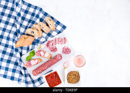 Salame su una lavagna bianca e un background in pietra, un bicchiere di vino rosato e vari snack. Spazio libero per il testo. Panini con la ciabatta e fre Foto Stock