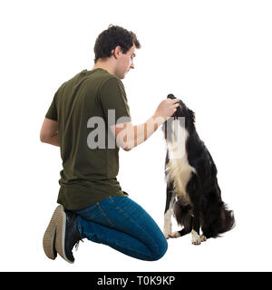 Ben addestrato Border Collie mangiare dal suo maestro mani. Giovane proprietario seduto sulle ginocchia alimentare un senzatetto cane affamato isolato su bianco backg Foto Stock