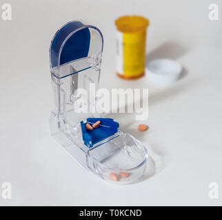 Su una superficie bianca possiamo vedere una pillola splitter, dosi dimezzate e un compresse farmaceutiche contenitore. Foto Stock