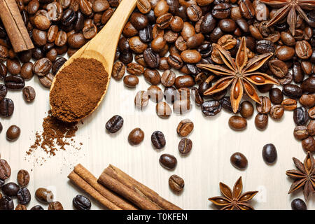 Chicchi di caffè tostati con spezie aromatiche anice stellato e bastoncini di cannella sul tavolo luminoso, vista dall'alto. Foto Stock