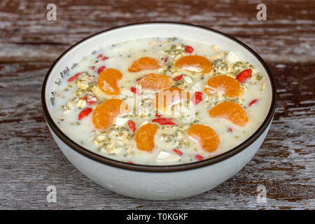 La colazione era fresca di muesli, yogurt, dadi, goji bacche, chia semi e mandarino. Muesli con frutti e bacche in un recipiente su un sfondo di legno, chiudi Foto Stock