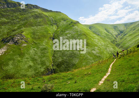 Giovane donna escursionismo in il sentiero alla grotta Arpea, spettacolare piega anticlinale piega circondato da verdi pascoli nei Pirenei francesi (Estérençuby, Francia) Foto Stock