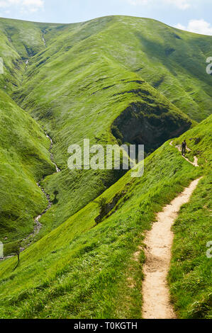 Giovane donna escursionismo in il sentiero alla grotta Arpea, spettacolare piega anticlinale piega circondato da verdi pascoli nei Pirenei francesi (Estérençuby, Francia) Foto Stock