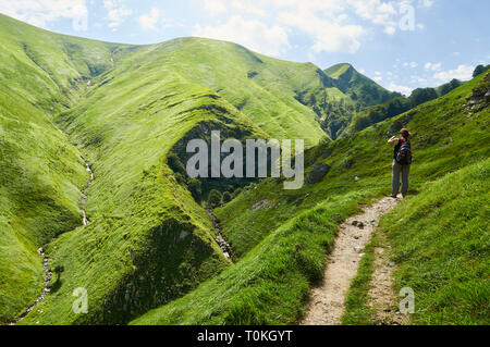 Giovane donna in una scia di fotografare Arpea grotta, spettacolare piega anticlinale piega circondato da verdi pascoli nei Pirenei francesi (Estérençuby, Francia) Foto Stock