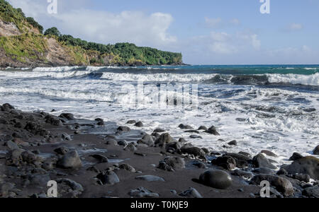 Spiaggia di sabbia nera: una laminazione, zangolatura surf lucidi rocce laviche e depositi di sabbia nera su una spiaggia nelle isole Hawaii. Foto Stock