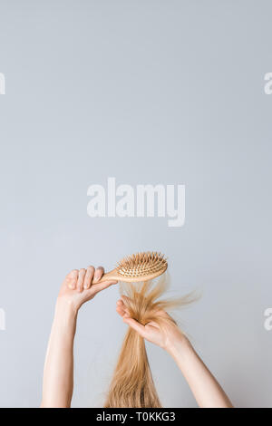 Giovane donna spazzolare i capelli biondi con una spazzola in legno. Immagine con copia spazio. Foto Stock