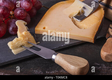 Giallo, hardware e delizioso formaggio da Paesi Bassi servita con uve su un piatto di pietra. Foto Stock