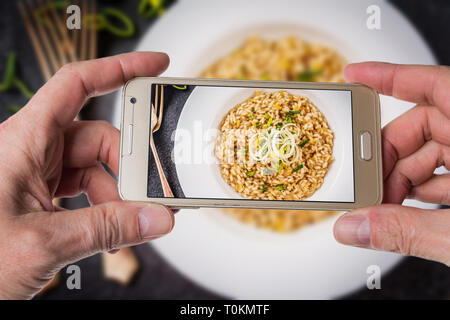 L'uomo prendendo foto di riso arborio risotto con porri sul tavolo bianco Foto Stock