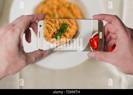 L'uomo prendendo foto di rosso il risotto con pomodoro e basilico su piastra bianca Foto Stock