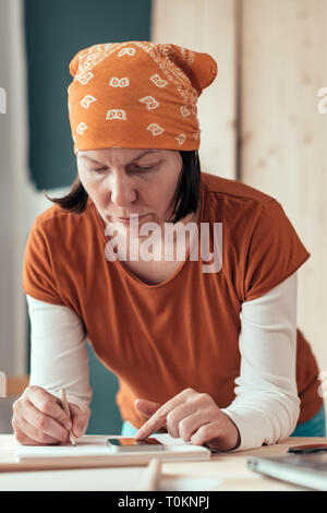 Falegname femmina con il fazzoletto di testa facendo il calcolo finanziario in falegnameria officina di falegnameria Foto Stock