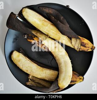 3 su banane mature su piastra nera Foto Stock