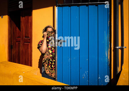 La donna nasconde il suo volto dietro una sciarpa davanti a casa sua, Colombo, Sri Lanka Foto Stock