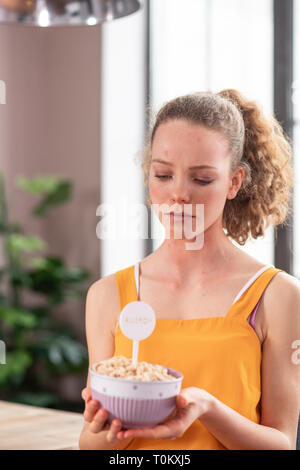 Addolorato giovane donna indossa grembiule giallo e guardando sul recipiente Foto Stock