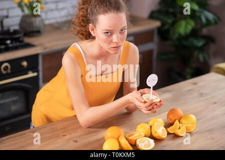 Ricci sconvolto dai capelli donna che indossa di colore giallo brillante vestito e guardando il limone Foto Stock