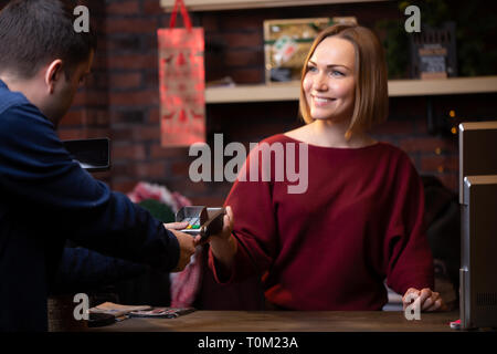 Foto del venditore sorridente donna in piedi dietro il registratore di cassa e acquirente maschio dal retro Foto Stock