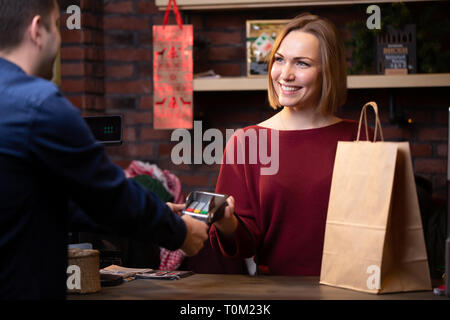 Immagine del venditore sorridente donna in piedi dietro il registratore di cassa e acquirente maschio dal retro Foto Stock