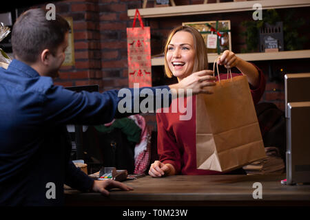 Immagine del venditore sorridente donna dando sacchetto di carta a maschio Foto Stock