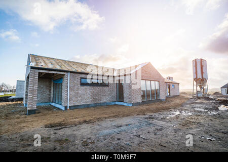 Nuova casa di mattoni in un cantiere con un grande silo al mattino Foto Stock