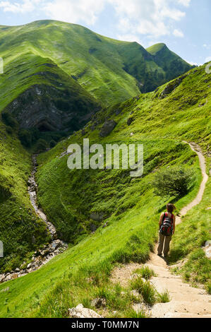 Giovane donna escursionismo in il sentiero alla grotta Arpea, spettacolare piega anticlinale piega cavallo rifugio circondato da verdi pascoli nei Pirenei (Estérençuby, Francia) Foto Stock