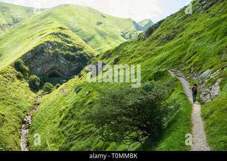 Giovane donna escursionismo in il sentiero alla grotta Arpea, spettacolare piega anticlinale piega cavallo rifugio circondato da verdi pascoli nei Pirenei (Estérençuby, Francia) Foto Stock