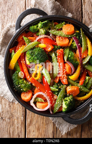 Stir fry di verdure con sesamo close-up in una ciotola sul tavolo, stile rustico. Verticale in alto vista da sopra Foto Stock