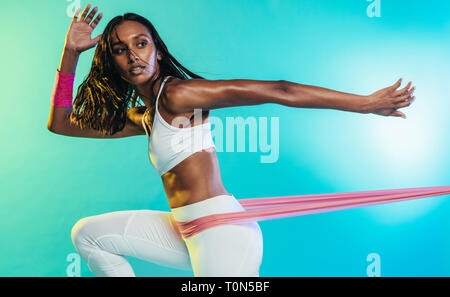 Giovane donna forte che fa esercizi con fascia di resistenza su sfondo colorato. fitness femminile che si allena con la fascia di resistenza. Foto Stock