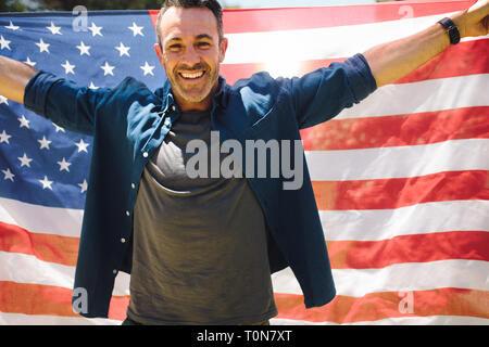 Ritratto di un uomo sorridente tenendo una grande bandiera americana dietro di lui. L uomo per celebrare una occasione portando la bandiera americana dietro di lui. Foto Stock