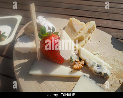 Assortimento di formaggi decorati con una perfetta fragola su un tagliere di legno Foto Stock