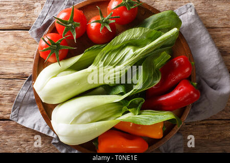 Ortaggi freschi assortiti baby bok choi, pomodori e peperoni close-up su una piastra su un tavolo di legno. Parte superiore orizzontale vista da sopra Foto Stock