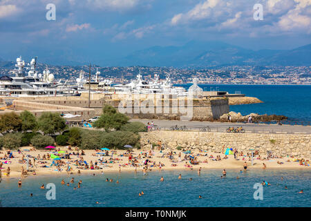 Persone su Plage de la Gravette - famosa e rinomata spiaggia di sabbia vicino alla città vecchia marina e yacht di lusso in background in Antibes. Foto Stock